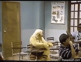 a group of people are sitting at desks in a classroom with a mascot sitting in a chair .