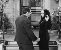 a black and white photo of a man and woman dancing in front of a house .