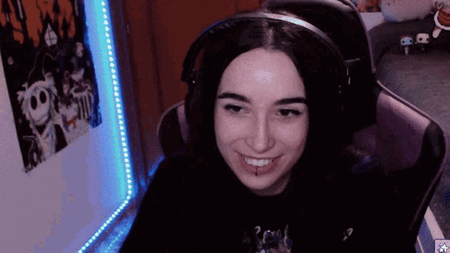 a woman wearing headphones is smiling in front of a wall with a nightmare before christmas poster