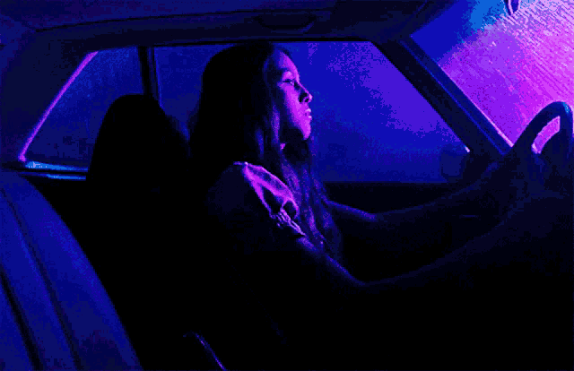 a woman is driving a car with purple lights