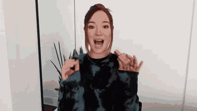 a woman in a tie dye sweater is holding a bottle of perfume and making a funny face .
