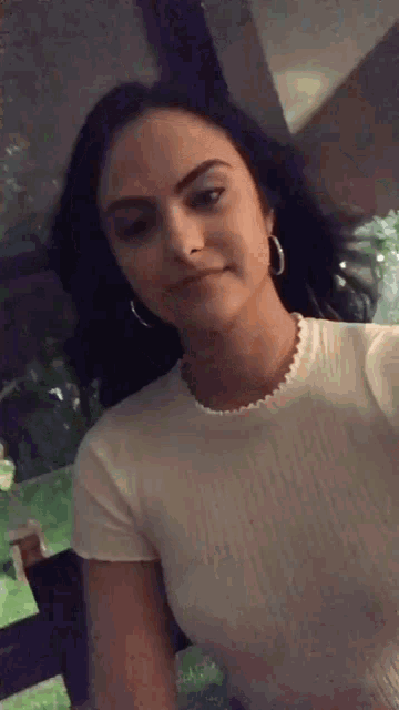 a woman is taking a selfie with her phone while wearing a white shirt and hoop earrings .