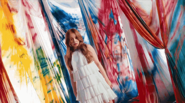 a woman in a white dress is standing in a room with colorful fabrics