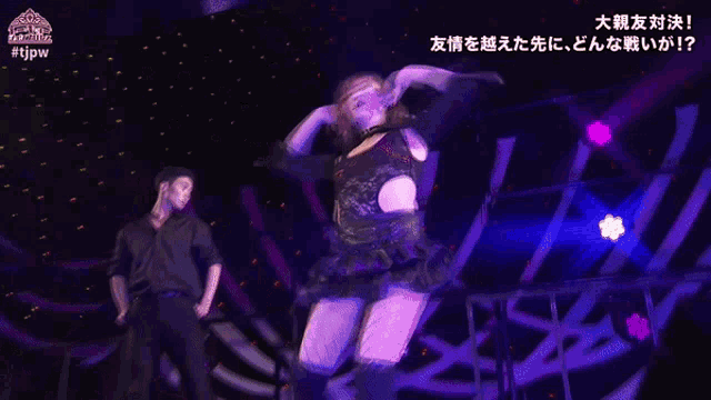 a woman in a black lace top is dancing on a stage with a man in a black shirt behind her