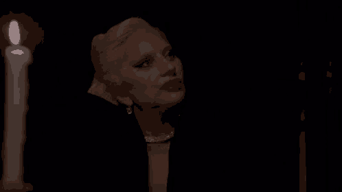 a woman in a black dress is standing next to a lit candle in a dark room .