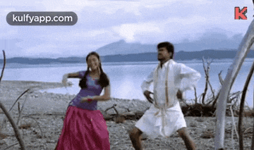 a man and a woman are dancing on the beach near a body of water .