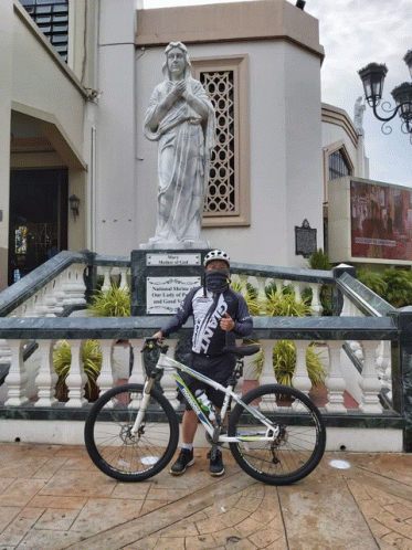 a man wearing a giant shirt stands next to a bicycle in front of a statue