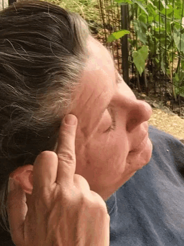 a woman holds her finger to her ear while making a middle finger gesture