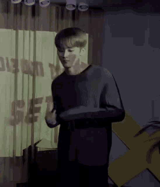 a man in a black shirt is standing in front of a yellow sign in a dark room .