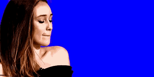 a woman in a black off the shoulder top is making a funny face in front of a blue background .