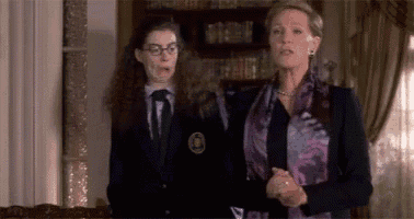 two women are standing next to each other in a room . one of the women is wearing a purple scarf .