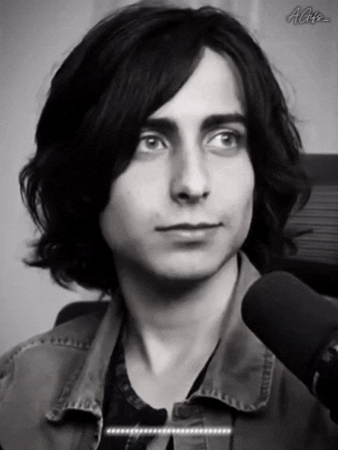 a black and white photo of a young man with long hair in front of a microphone with the letters ac on the bottom