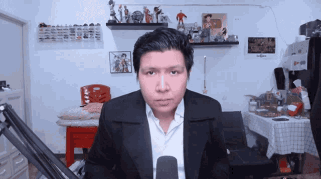 a man in a suit stands in front of a microphone in a messy room