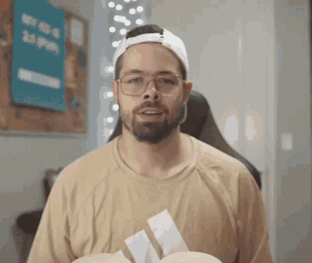 a man wearing glasses and a baseball cap is holding a tissue .