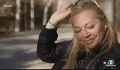a woman in a black jacket is smiling and touching her head .