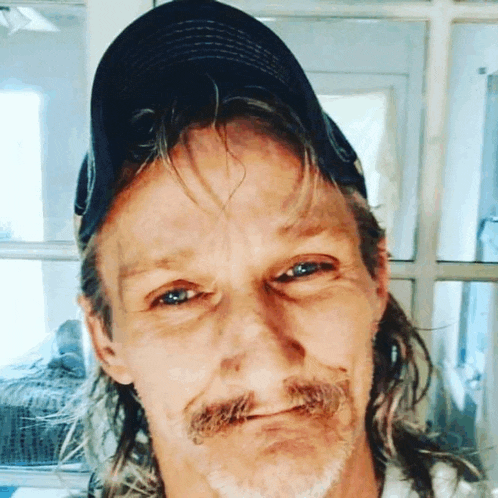 a man with long hair and a beard is wearing a baseball cap