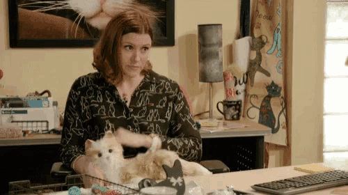 a woman sits at a desk with two cats on her lap