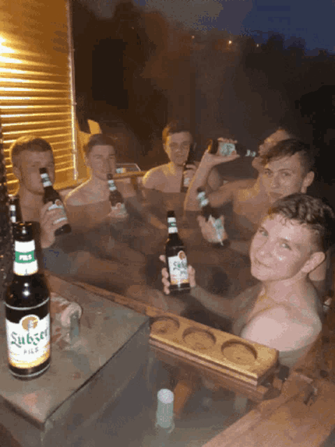 a group of young men in a bathtub holding up bottles of stubser