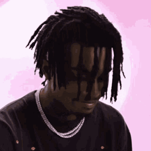 a man with dreadlocks and a necklace is looking down .