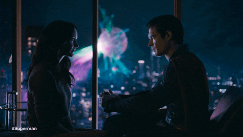 a man and a woman are looking at each other in front of a window with #superman on the bottom