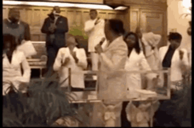 a group of people in white suits are clapping and singing in a church