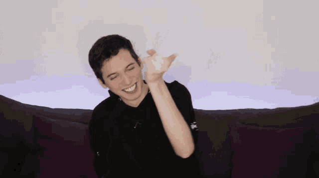 a young man is sitting on a couch with purple pillows and smiling