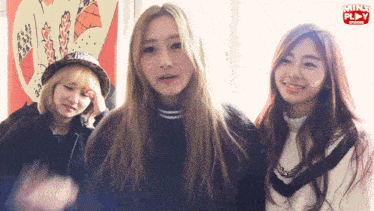 three girls are standing next to each other in front of a minx play poster