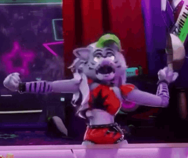 a tiger mascot is standing on a stage in a room holding a guitar .