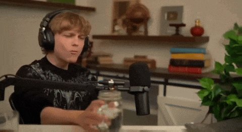 a young man wearing headphones is sitting in front of a microphone holding a jar .