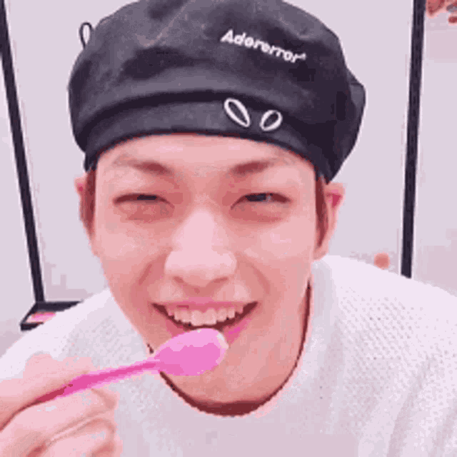 a young man wearing a black beret is eating a pink spoon .