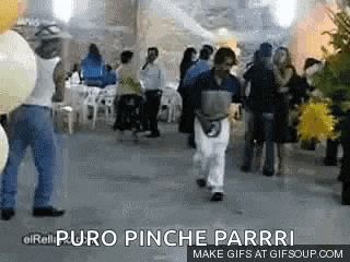 a group of people are dancing in a room with balloons and a man is walking in the middle of the room .