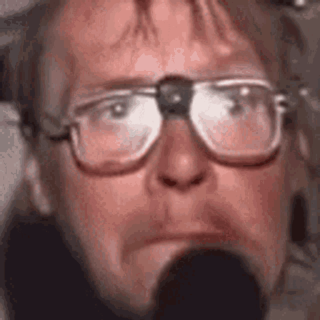 a man wearing glasses is talking into a microphone and making a funny face .