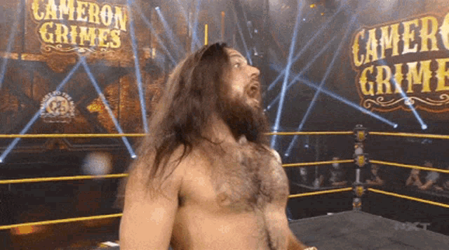 a shirtless wrestler in a ring with cameron grimes written on the wall behind him