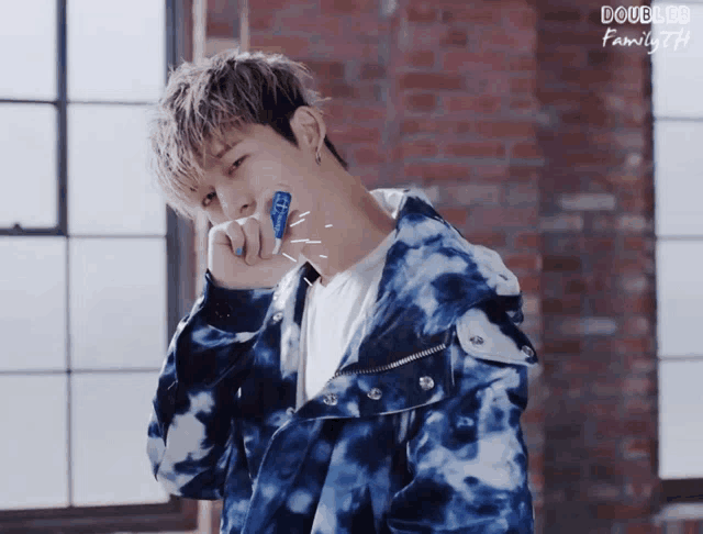 a young man in a blue tie dye jacket holds a toothbrush in his mouth