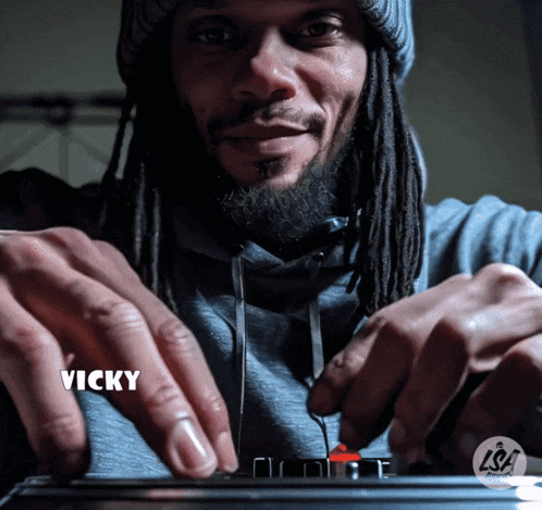 a man with dreadlocks and the name vicky is playing a musical instrument
