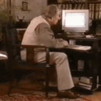 an elderly man sits in front of a computer monitor