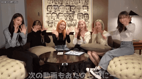 a group of girls are sitting on a couch with their hands in the air in front of a painting of faces