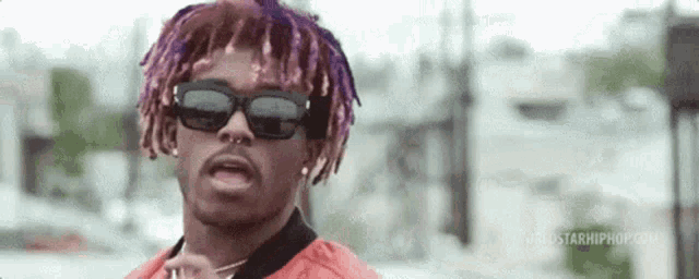 a man with purple dreadlocks and sunglasses is standing in front of a city .