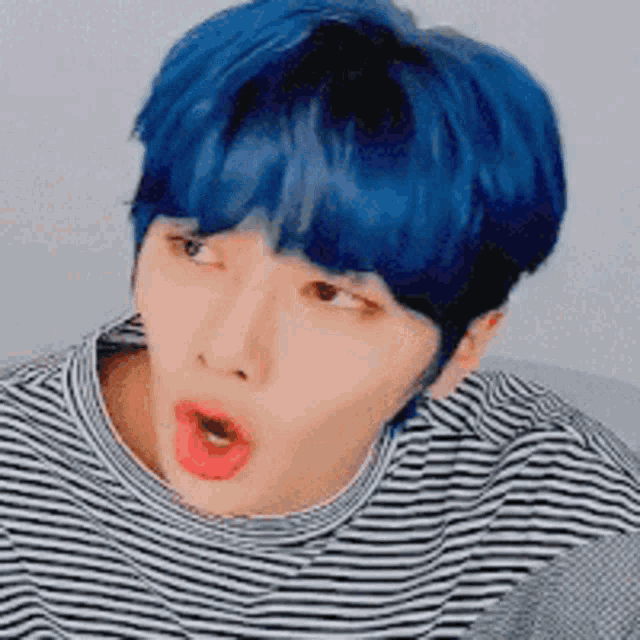 a boy with blue hair and a striped shirt is making a funny face .