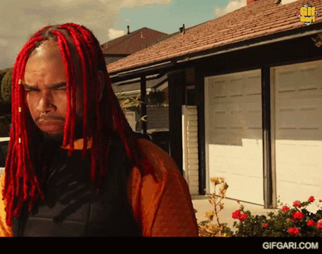 a man with red dreadlocks is standing in front of a garage door with gifgari.com written on the bottom