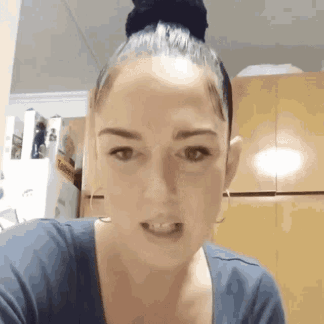 a woman with her hair in a bun is looking at the camera while wearing a blue shirt .