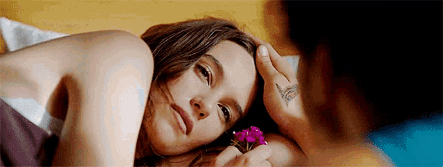 a woman is laying in bed with a man holding a flower .