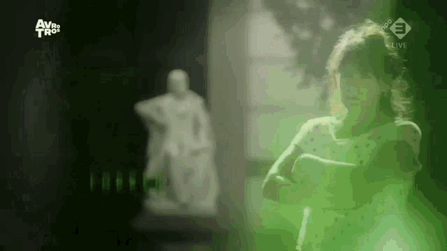 a woman is standing in front of a statue in a dark room with a green background .