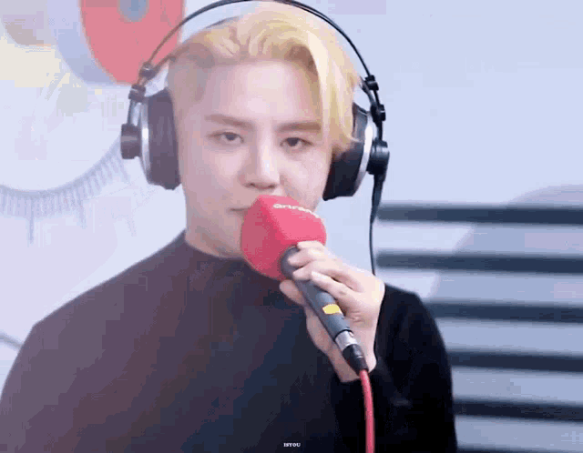a man with blonde hair is wearing headphones and holding a red microphone .