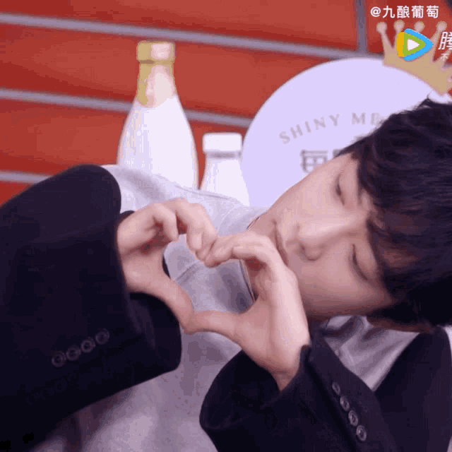 a man making a heart shape with his hands in front of a shiny me sign