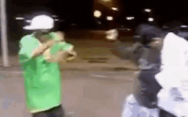a man in a green shirt and a white hat is dancing on the street .