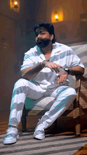 a man with a beard sits in a chair with his hands on his hips