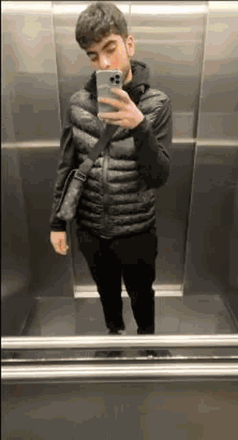 a man is taking a selfie in an elevator while holding a cell phone .