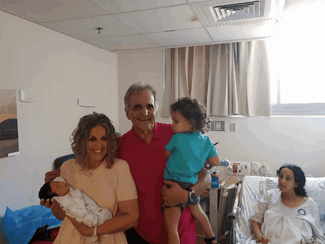 a family poses for a picture in a hospital room while a pregnant woman sits in a hospital bed