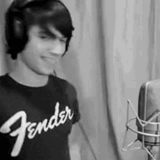 a man wearing a fender t-shirt is standing in front of a microphone .